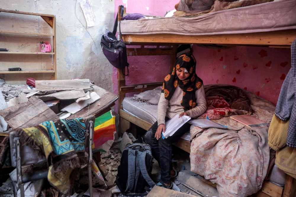 A girl sorts through her school notes as she sits on a bed in her damaged room in the aftermath of Israeli bombardment on an apartment building in the Bureij camp for Palestinian refugees in the central Gaza Strip on January 7, 2025. — AFP pic