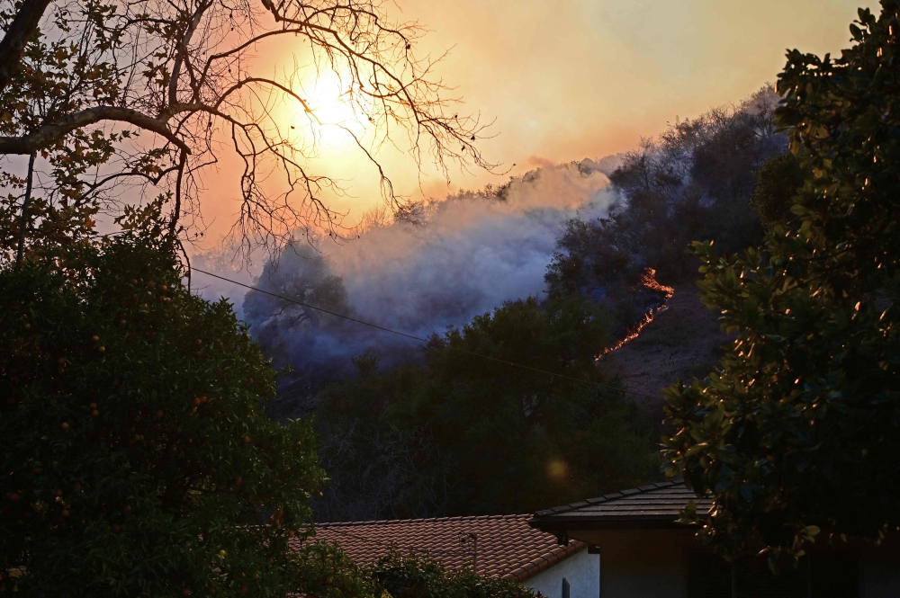 Smoke from flames rises behind homes in the Mandeville Canyon neighborhood of Los Angeles, California, on January 11, 2025, as the Palisades Fire continues to burn. — AFP pic