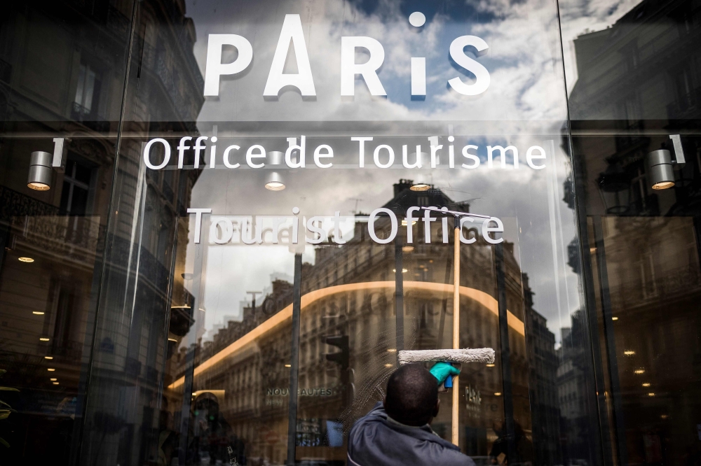 A window cleaner wipes the glass door of the Paris' tourist office, showing its logo and buildings reflection on October 20, 2016 in Paris. — AFP pic