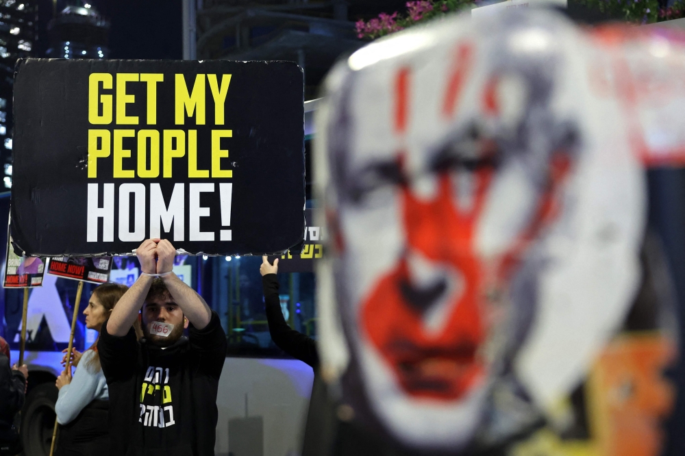 A demonstrator raises a placard during an protest calling for action to secure the release of Israelis held hostage in Gaza since the October 2023, in front of the Israeli defence ministry in Tel Aviv January 14, 2025. — AFP pic