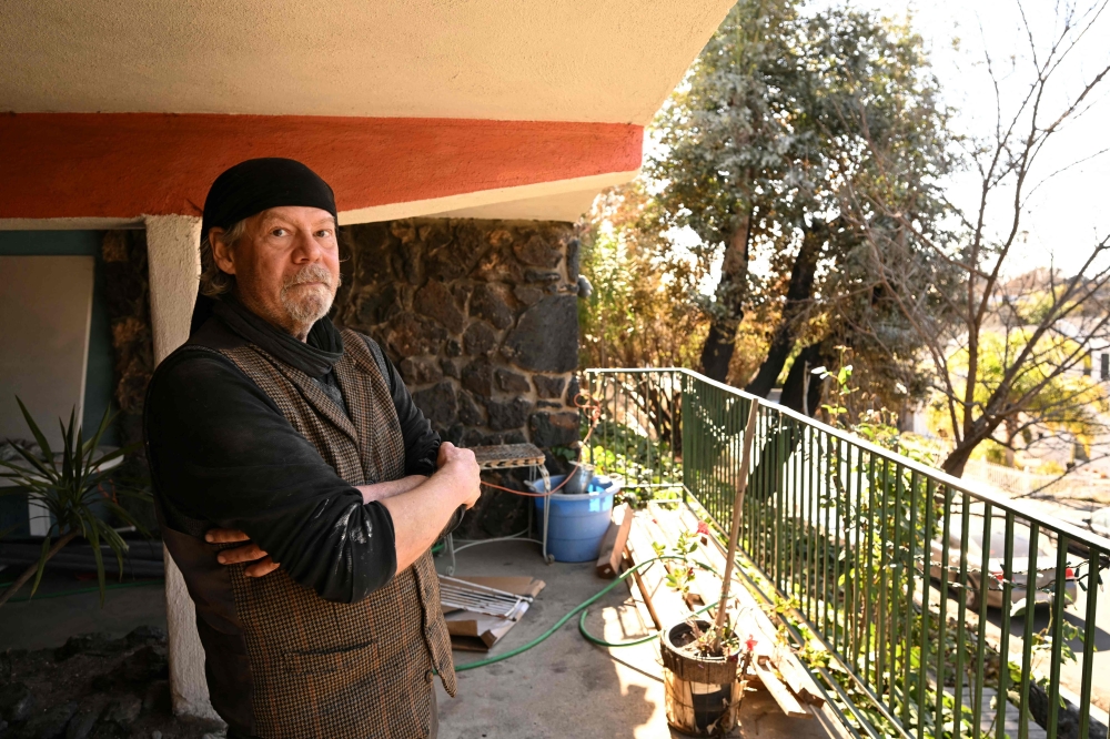 Jeff Ridgway poses next to a charred eucalyptus tree (back C) that he extinguished with a hose at the building where he lives and serves as property manager. — AFP pic