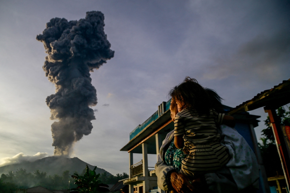 A woman and child watch as volcanic ash billows into the sky during the eruption of Mount Ibu, observed from Duono Village in West Halmahera, North Maluku province. — AFP pic
