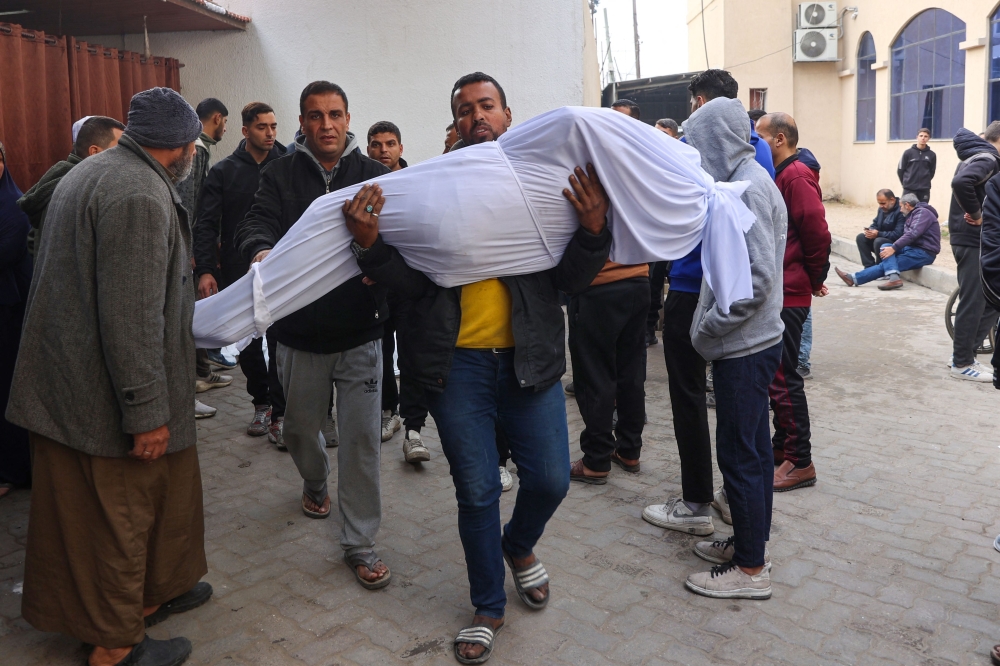 A man carries the shrouded body person killed in Israeli strikes in Gaza City the previous night, at Al-Ahli Arab hospital, also known as the Baptist hospital, on January 16, 2025, following a truce announcement amid the war between Israel and the Palestinian Hamas movement. — AFP pic