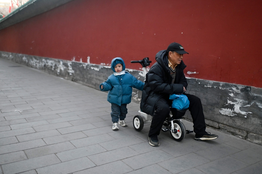 An adult rides a children’s tricycle, as a child walks alongside, at a park in Beijing January 16, 2025. China’s birth rates have been falling for decades as a result of the one-child policy China implemented from 1980 to 2015 as well as rapid urbanisation. — AFP pic