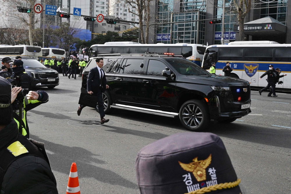 Security officials run alongside a motorcade believed to be transporting impeached South Korea President Yoon Suk Yeol to the Seoul Western District Court in Seoul on January 18, 2025, to attend a hearing which will decide whether to extend his detention as investigators probe his failed martial law bid. — AFP pic
