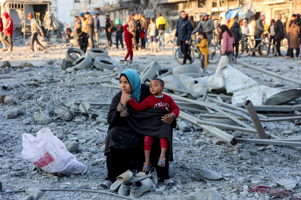 A woman sits with a child with salvaged footwear amidst debris and rubble at the site of Israeli bombardment on a residential block in Jalaa Street in Gaza City on January 14, 2025. — AFP pic