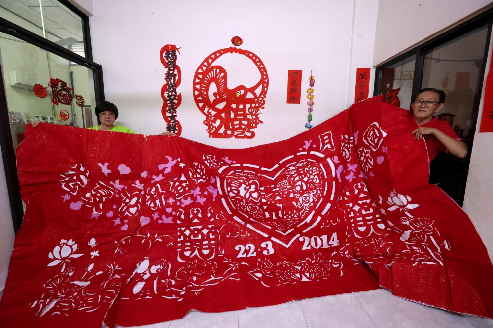 The Koays hold up a 4mx2m paper cut decoration made for their son’s wedding in 2014. — Bernama pic