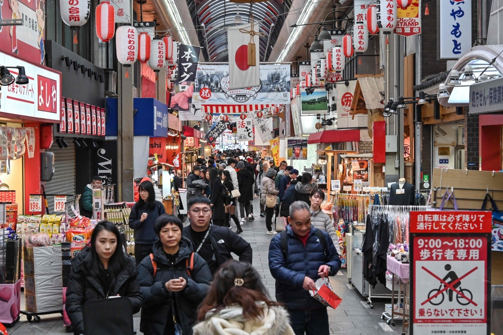 Tourists walk past stalls selling seafood, Kobe beef and other souvenirs at the popular Kuromon Ichiba market in central Osaka on January 19, 2025. — AFP pic