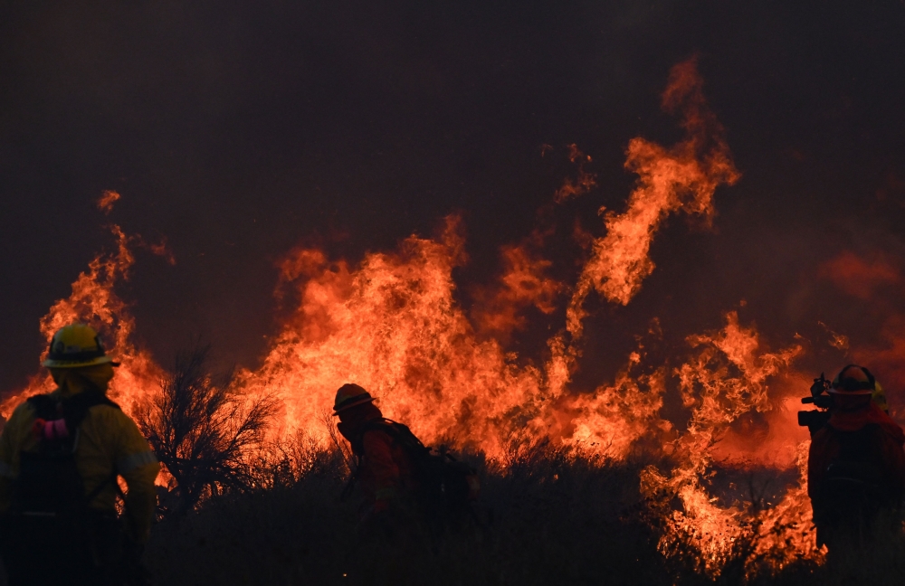 An inmate crew led by firefighters light backfires near power lines as smoke from the Hughes Fire fills the sky in Castaic. — Pic by AFP