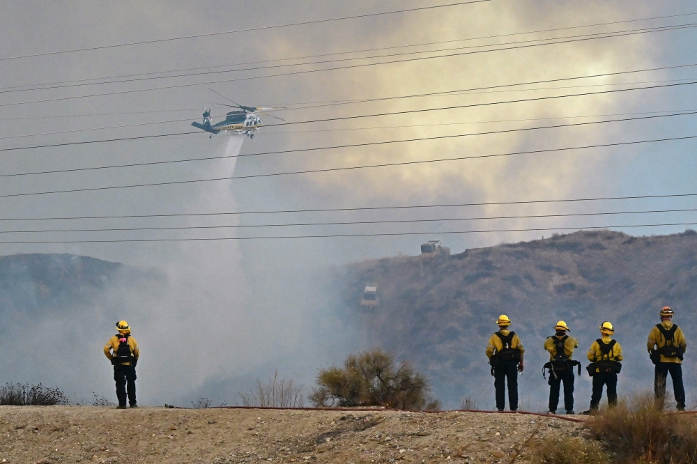 Firefighters watch as a helicopter drops water as the Hughes Fire burns near Castaic. — Pic by AFP