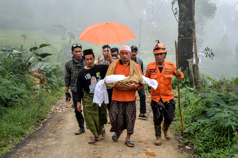A father carries his one-and-a-half-year-old daughter, who died in a landslide triggered by heavy rains in Kasimpar village, Central Java. — Pic by AFP 