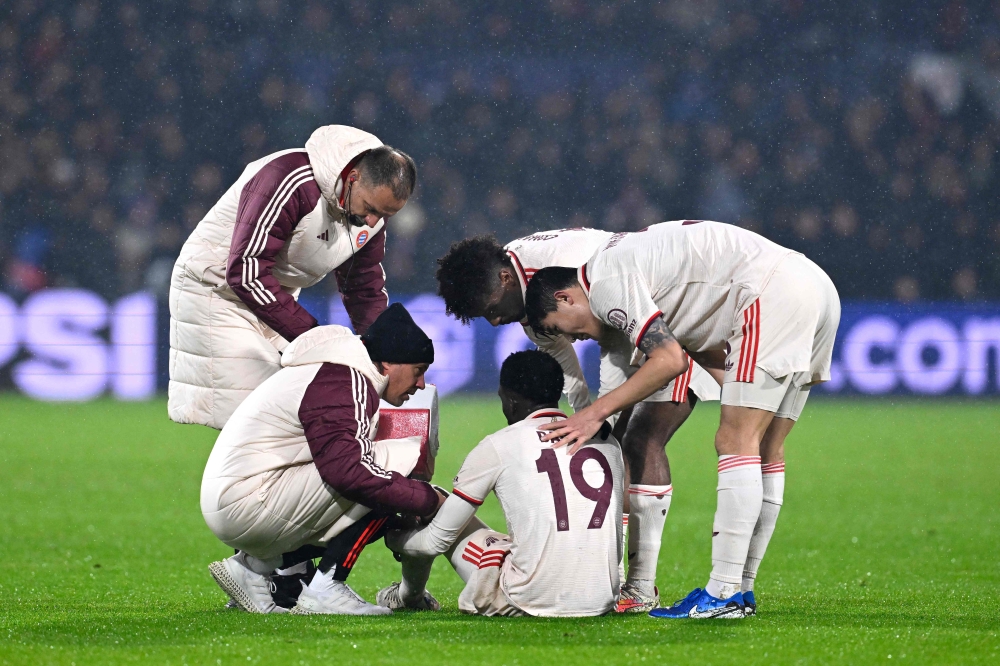 Bayern Munich's players and phyio's comfort Bayern Munich's Canadian defender Alphonso Davies (C) as he sits on the ground injured during the match. — AFP pic