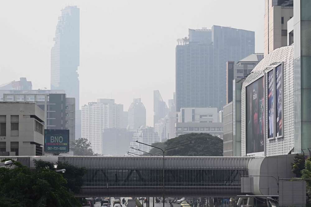 People are seen walking through a pedestrian bridge amidst high levels of air pollution in Bangkok January 24, 2025. — AFP pic