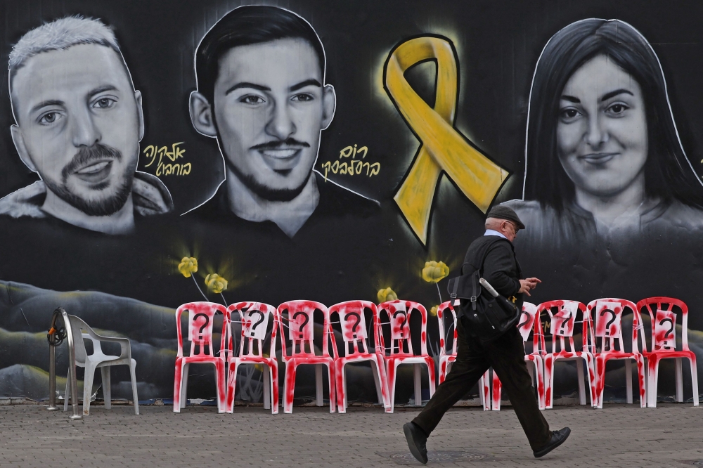 A pedestrian runs past a mural with the portraits of Israeli hostages held in the Gaza Strip since the October 7, last year. — AFP pic