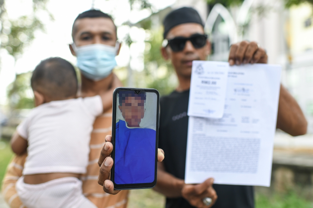 Ahmad Mudzakkir Ahmad Mukri, 37 (left), shows a photo of his son who experienced severe bleeding after undergoing circumcision during a mass circumcision programme yesterday. — Bernama pic