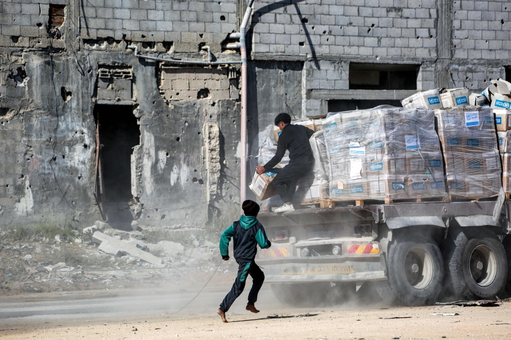A boy chases one of the trucks carrying humanitarian aid by the United Nations Relief and Works Agency for Palestine Refugees (UNRWA) coming in from the Kerem Shalom border crossing and arriving in al-Shoka, east of Rafah in the southern Gaza Strip. — AFP pic