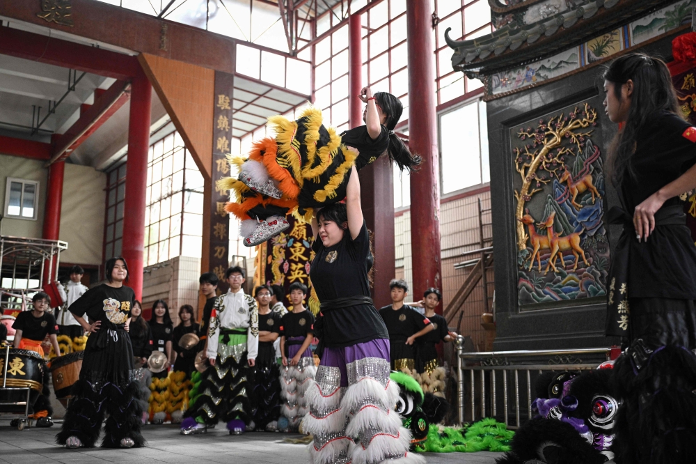 Lin Xinmeng holding a female lion dancer during a practice session. — AFP pic