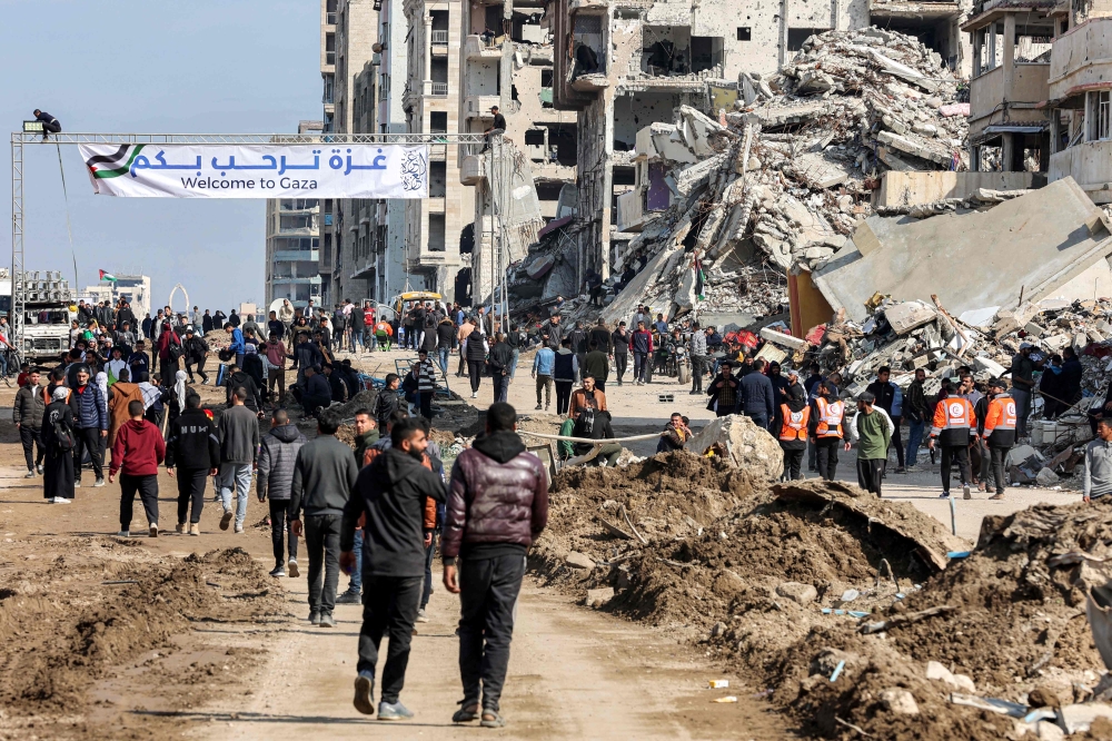 People gather by a banner welcoming people near the rubble of a collapsed building along Gaza's coastal al-Rashid Street for people to cross from the Israeli-blocked Netzarim corridor from the southern Gaza Strip into Gaza City on January 26, 2025. — AFP pic