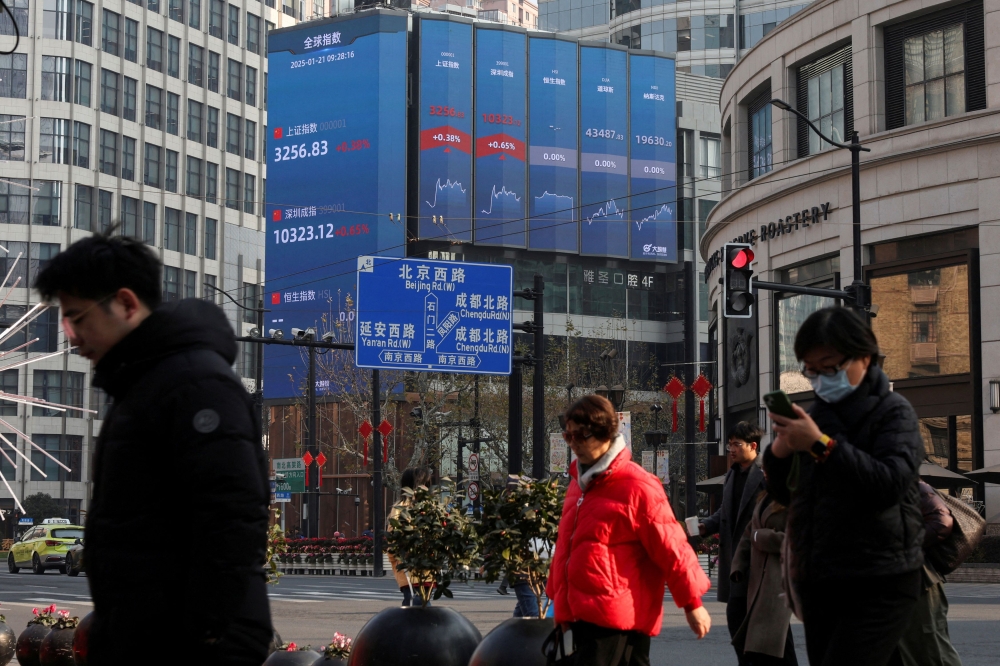 Pedestrians wait for a street signal on a sidewalk as an electronic billboard shows the Shanghai and Shenzhen stock indexes in Shanghai, China January 21, 2025. — Reuters pic