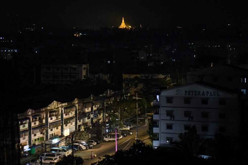 This photo taken on January 14, 2025 shows a man (down) riding his bike along a street, with the Shwedagon Pagoda seen in the background, during an electricity blackout in Yangon. — AFP pic