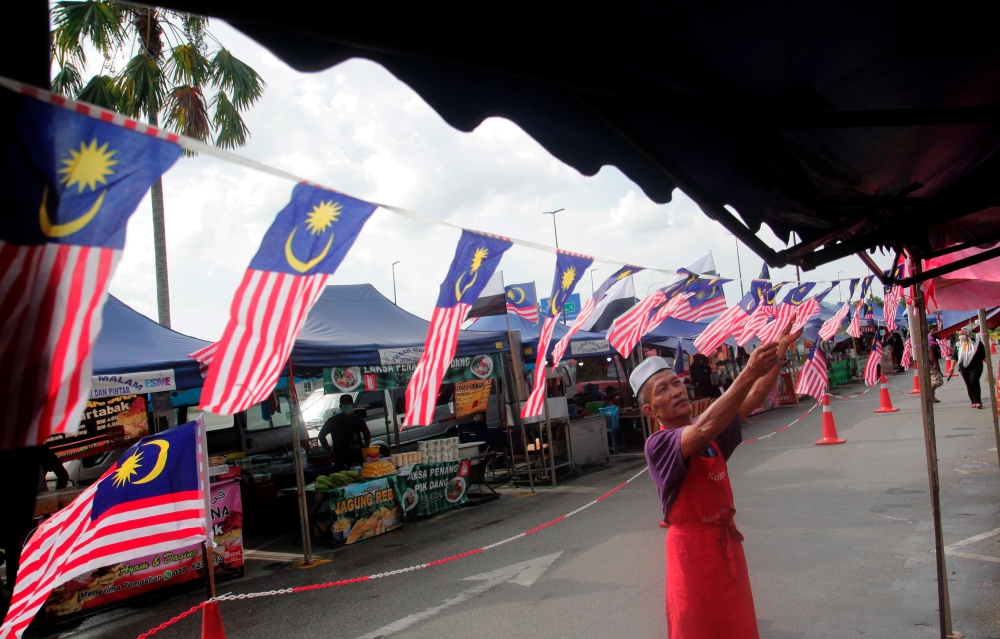 A man adjusts the rows of Jalur Gemilang installed at his stall during at Pasar Malam TMG Mall Tanjong Lumpur in Kuantan in this file picture dated August 21, 2022. According to a KRI report,  hawkers serve as a ‘safety valve’ for employment, providing livelihoods for individuals with limited capital, education, or skills and addressing poverty and income inequality. — Bernama pic