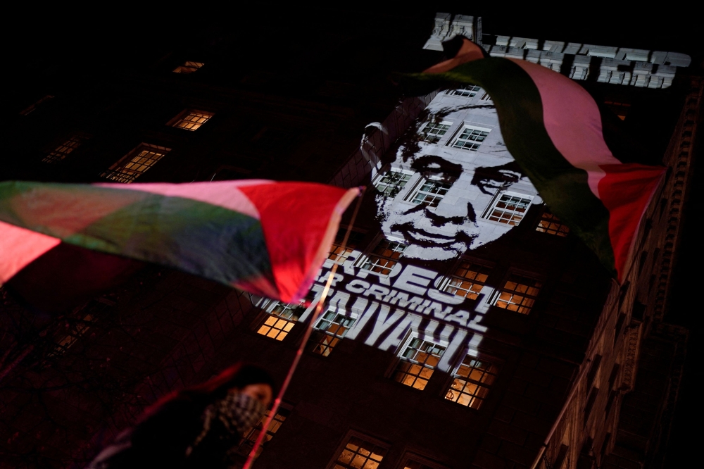 A pro-Palestinian demonstrator holds a Palestinian flag as the image of Israeli Prime Minister Benjamin Netanyahu is projected, with a message that reads 