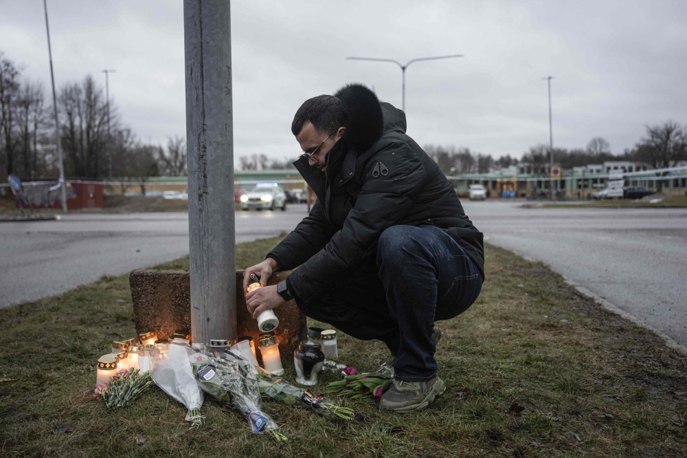 A man lights candles at a makeshift vigil in Orebro, Sweden, on February 5, 2025 after a shooting at the adult education center Campus Risbergska school, where eleven people were killed. — AFP pic