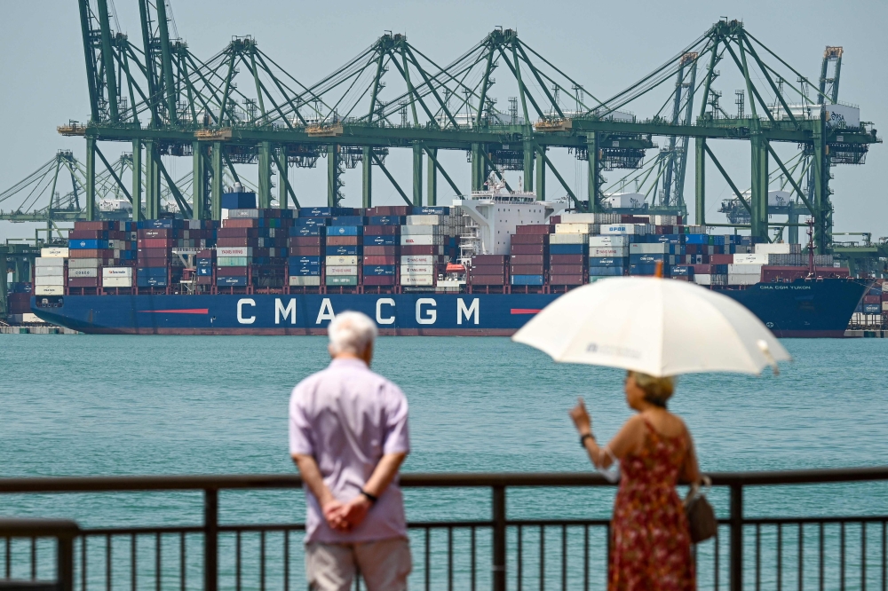 People walk along the water as a cargo ship is seen docked at Pasir Panjang port terminal in Singapore on February 3, 2025. — AFP pic