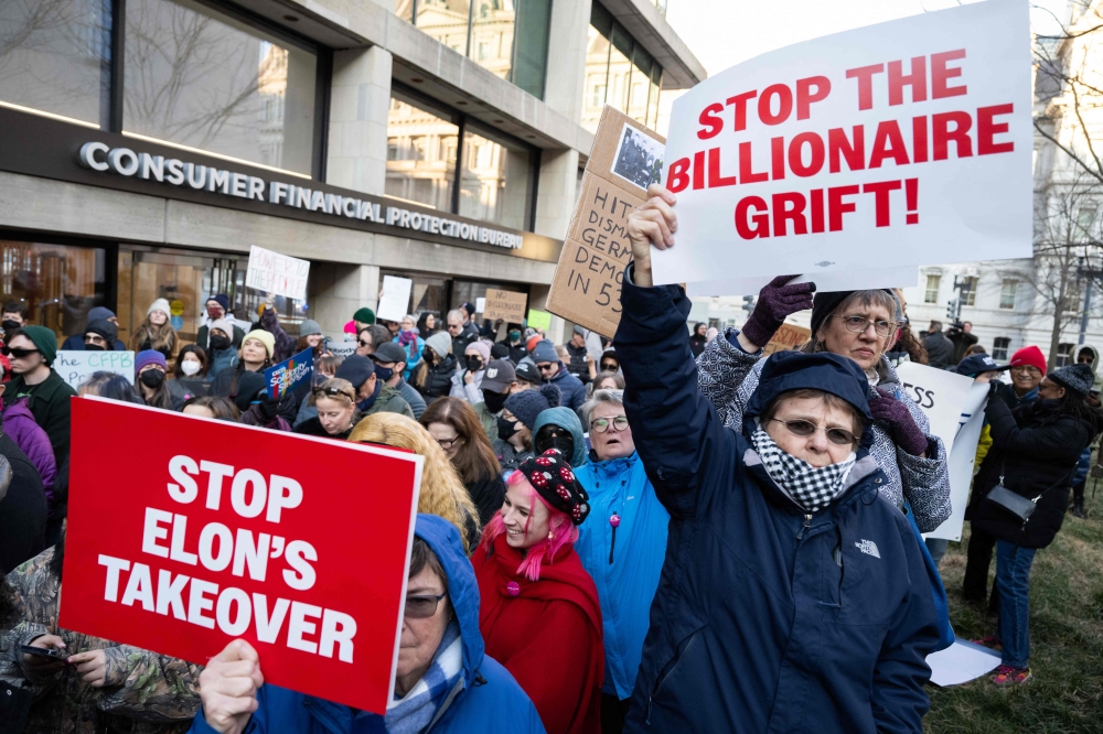 Demonstrators hold signs as they protest against US President Donald Trump and DOGE Elon Musk's anticipated plan to close the Consumer Financial Protection Bureau in front of the CFPB headquarters in Washington, DC, February 10, 2025. Democrats announced a new platform for US whistleblowers yesterday as they launched the latest front in their rearguard against efforts by Musk to gut federal spending. — AFP pic