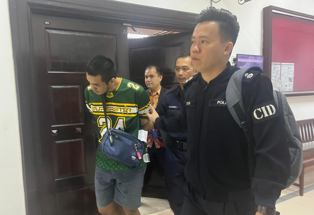 Police escort Mohd Nur Rakib after the proceedings at Kuching Court Complex here today. — The Borneo Post pic