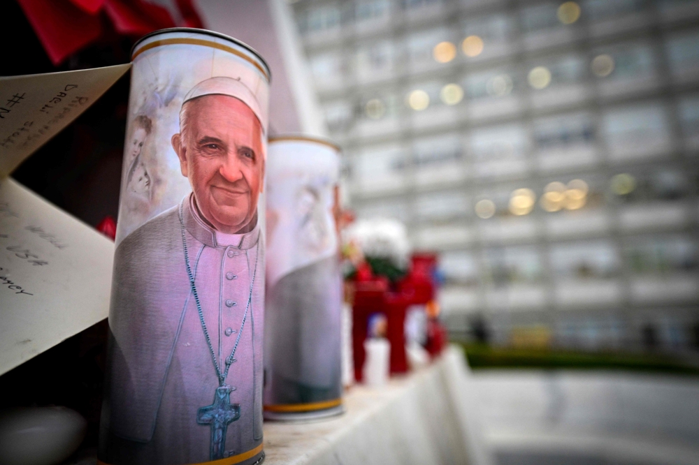 A candle with a portrait of Pope Francis is set at the bottom of a statue of Pope John Paul II outside the Gemelli hospital where Pope Francis is hospitalised for tests and treatment for bronchitis in Rome, on February 19, 2025.  — AFP pic