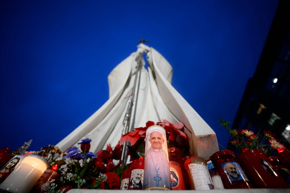 Candles are set at the bottom of a statue of Pope John Paul II outside the Gemelli hospital where Pope Francis is hospitalised for tests and treatment for bronchitis in Rome, on February 19, 2025. — AFP pic