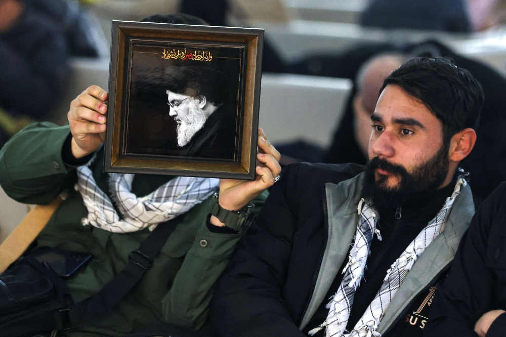 A Lebanese man holds a portrait of slain Hezbollah leader Hassan Nasrallah at Baghdad airport as he waits to board a flight to Beirut. — AFP pic