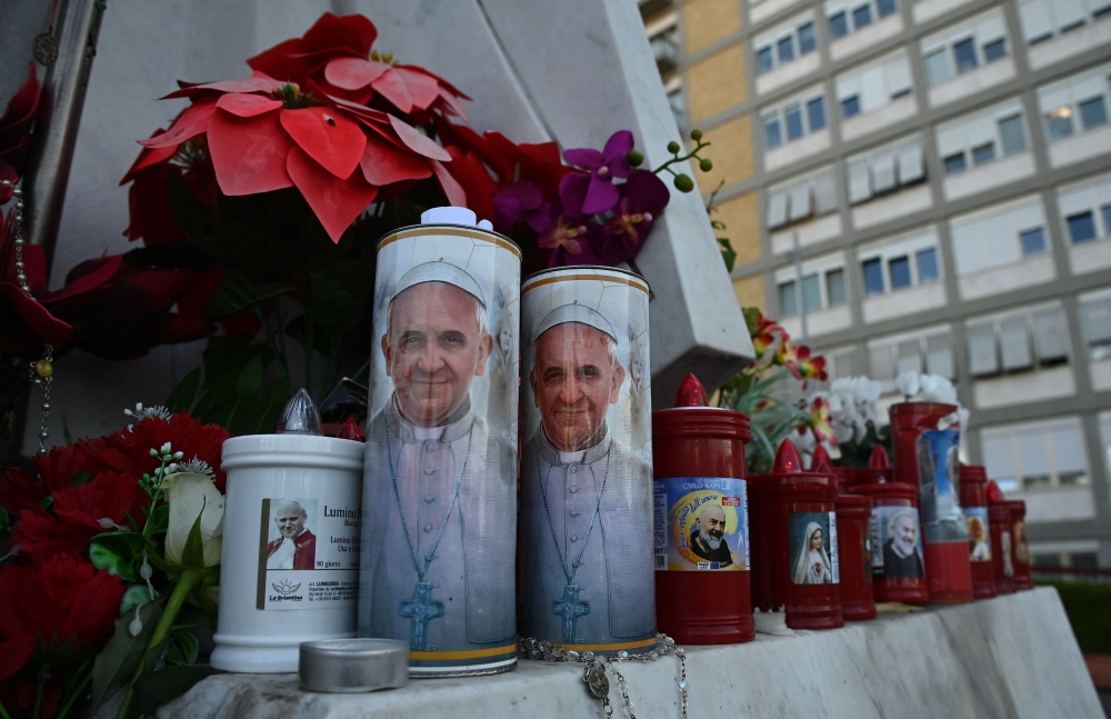 Candles with Pope Francis' portrait are set at the feet of a statue of John Paul II outside the Gemelli hospital where Pope Francis is hospitalized in Rome. —AFP pic