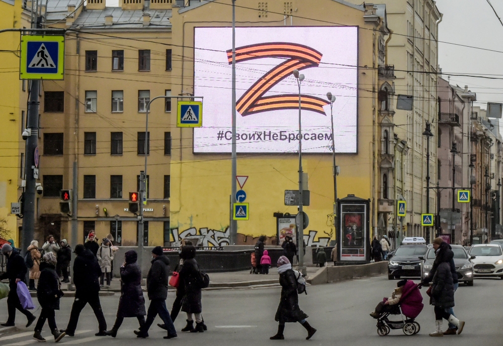 Pedestrians cross a street in front of a billboard displaying the symbol ‘Z’ in the colours of the ribbon of Saint George and a slogan reading: ‘We don’t give up on our people’, in support of the Russian armed forces, in Saint Petersburg, on March 7, 2022. — AFP pic