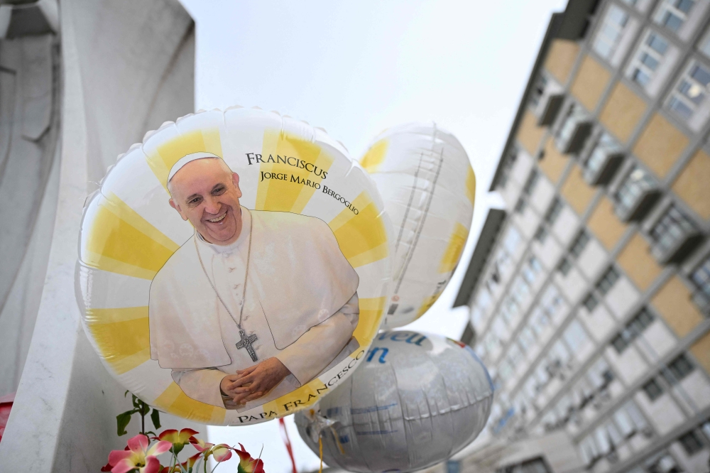 Balloons depicting Pope Francis are laid at the statue of John Paul II outside the Gemelli hospital where Pope Francis is hospitalized, in Rome on February 24, 2025. Pope Francis, in a critical condition in hospital with pneumonia, had a good night and was resting, the Vatican said on February 24, 2025. — AFP pic