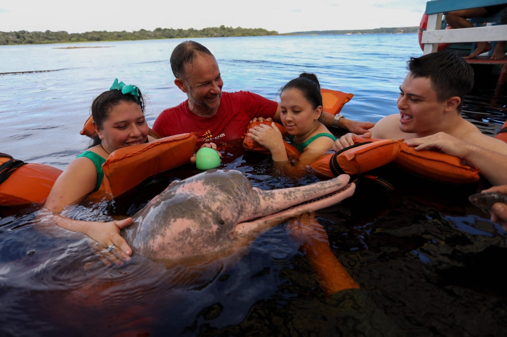 Physiotherapist Igor Simoes Andrade and young people with disabilities swim with pink dolphins (Inia geoffrensis) on the Rio Negro river in Iranduba, Amazonas state, Brazil, on February 20, 2025. — AFP pic