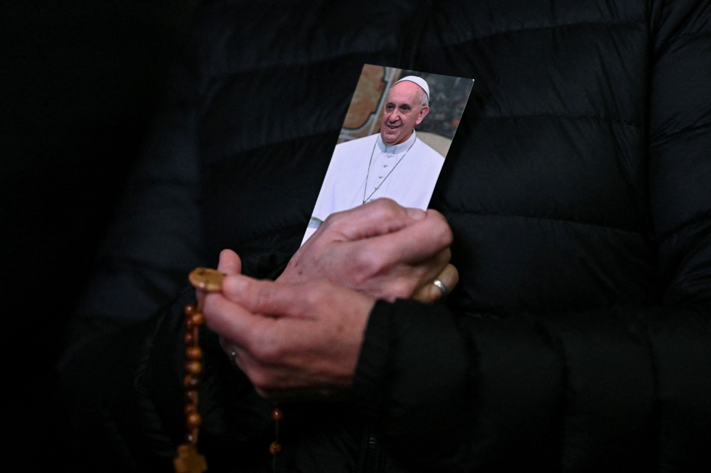 A person holds a picture of Pope Francis and a rosary during a prayer service at St Peter’s Square, as Pope Francis continues his hospitalisation, at the Vatican, February 25, 2025. — Reuters pic 