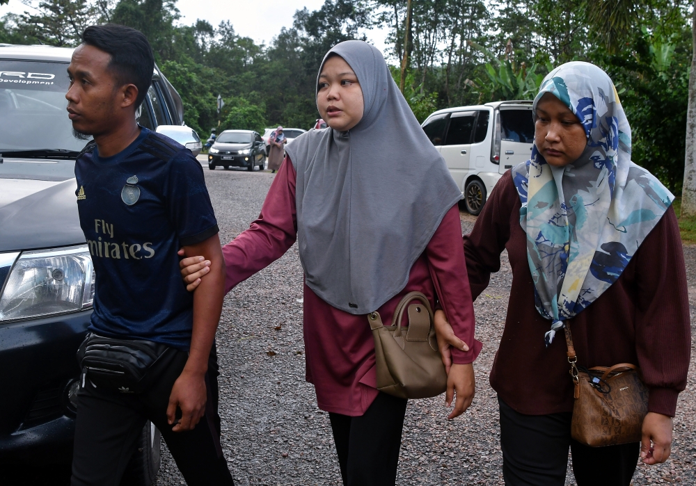 Mohd Nor Hafifi Saidi, 34, (left) with his wife Azean Nur Atikah Mohd Ramley, 34, (centre), accompanied by family members, arriving at the Tanah Merah Hospital Forensic Unit for the post-mortem process after their 19-month-old son, Hud Aryan Mohd Nor Hafifi, was found dead near the riverbank close to their home in Kampung Aira Kuala Tiga yesterday. — Bernama pic