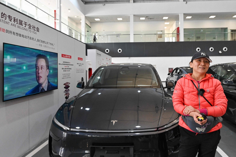 A woman stands next to her new Tesla Model Y car as a picture of US tech billionaire Elon Musk is seen displayed on a screen at Tesla's Xiedao delivery centre in Beijing on February 27, 2025. — AFP 