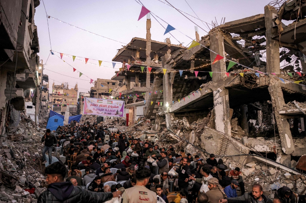 People gather for the iftar, or fast-breaking meal, on the first day of the Muslim holy fasting month of Ramadan in Jabalia in the northern Gaza Strip yesterday by the rubble of collapsed buildings that were destroyed during the war between Israel and Hamas, amid the ongoing truce.  – AFP