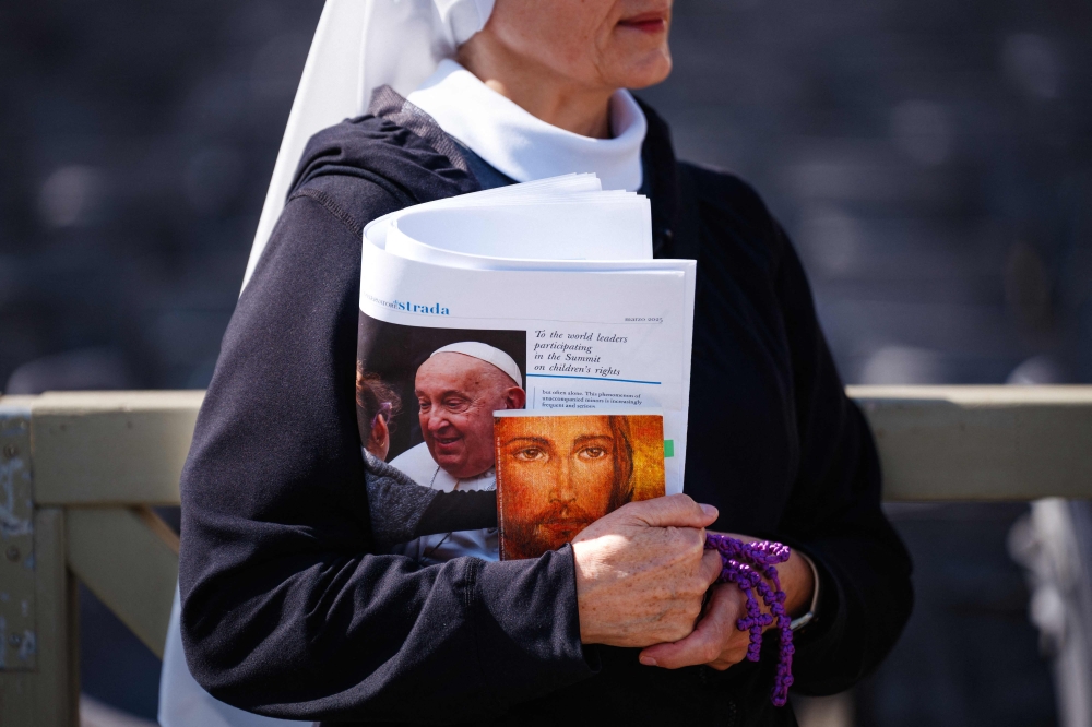 A nun walks with the ‘Osservatore Romano’ newspaper under her arm as Pope Francis is still hospitalised with pneumonia and will not lead the Angelus prayer, at St Peter’s square in The Vatican on March 2, 2025. — AFP pic
