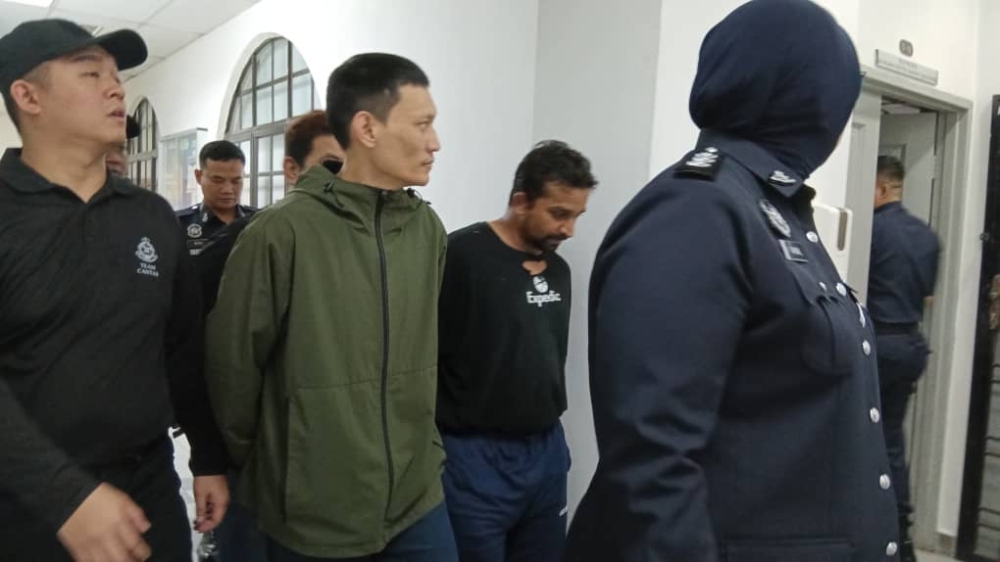 Accused Mohamad Haidar Abdullah (left, in green parka) and N. Klement Raj being escorted by policemen in the Johor Baru courthouse. Both later claimed trial to joint and separate charges for gang robbery, possession of firearms and imitation weapons at the Sessions Court today. — Picture by Ben Tan