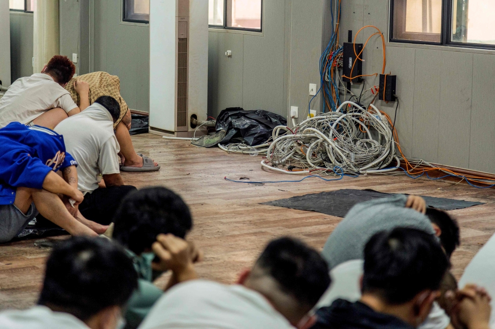 Alleged scam centre workers and victims sit next to dismantled IT and electronic appliances during a crackdown operation by the Karen Border Guard Force on illicit activity in Shwe Kokko in Myanmar's eastern Myawaddy township. — AFP pic