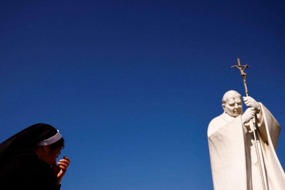 A nun prays near the statue of late Pope John Paul II outside Gemelli Hospital, where Pope Francis continues his treatment, in Rome. — Reuters pic