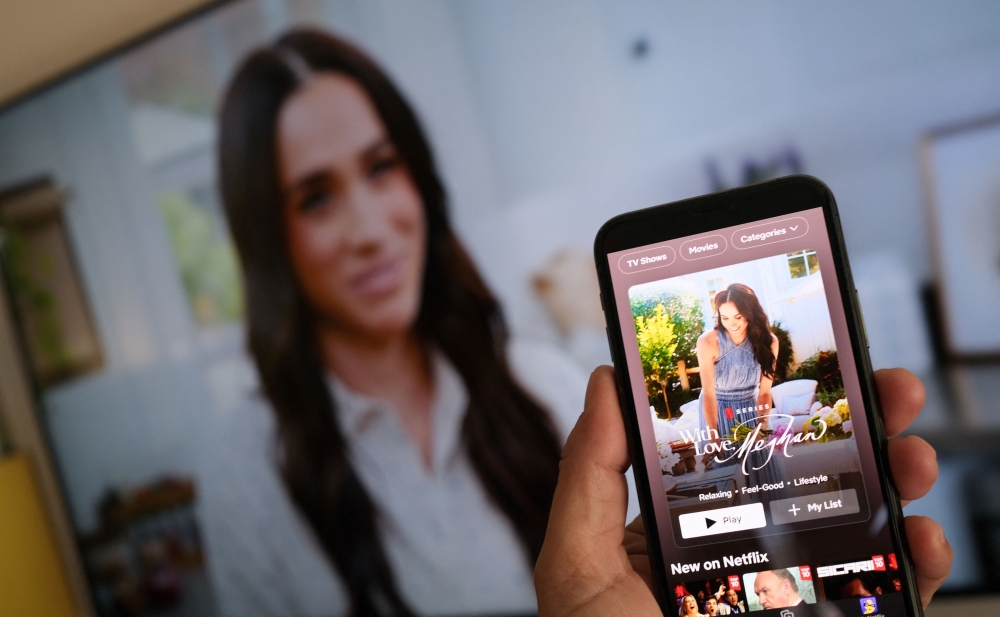 A person holds a smartphone displaying Netflix's new Meghan Markle show, ‘With Love, Meghan’, in front of a TV screen showing footage of the show, in Los Angeles, March 4, 2025. — AFP pic
