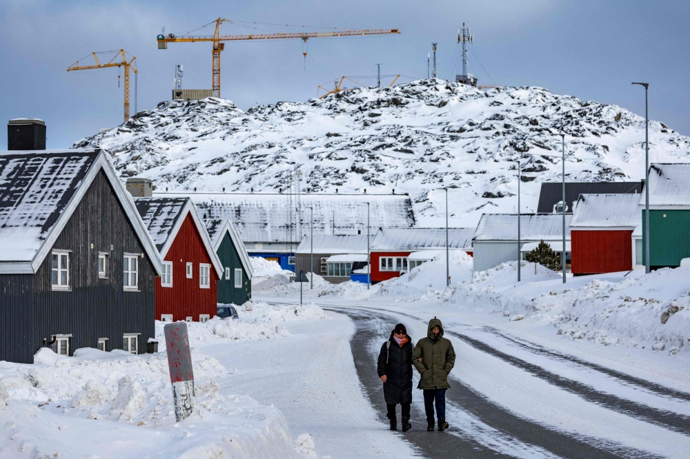 Construction cranes are seen behind a couple walking in Nuuk, Greenland, on March 6, 2025. Greenland, an autonomous Danish territory coveted by US President Trump and which votes on March 11, 2025 in legislative elections, is home to around 500 homeless people, or almost one percent of its population, according to a 2022 tally. — AFP pic
