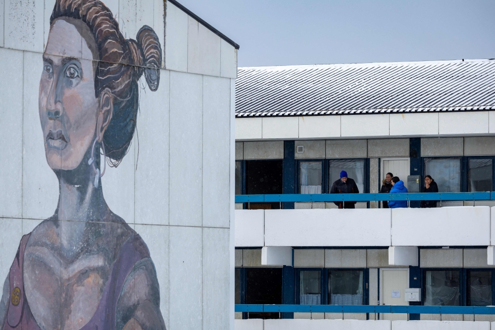 Residents share a cigarette next to a mural on a social housing estate in Nuuk, Greenland, on March 6, 2025. — AFP pic