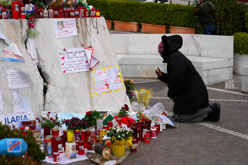 A person prays at the statue of John Paull II outside the Gemelli University Hospital where Pope Francis is hospitalised with pneumonia, in Rome on March 10, 2025. — AFP pic