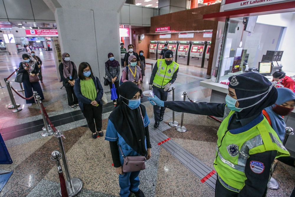Auxiliary police check the temperatures of commuters at KL Sentral during the 2020 movement control order. — Picture by Hari Anggara